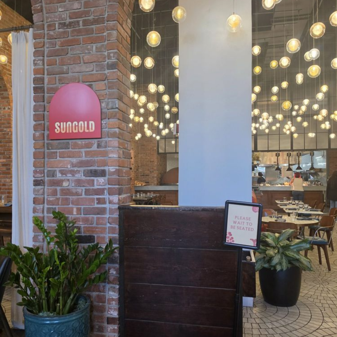 NYC Labor Day dining at Sungold restaurant with exposed brick walls, modern globe lights, red sign, and stylish contemporary design, culinary venue featured in daily things to do in NYC any day