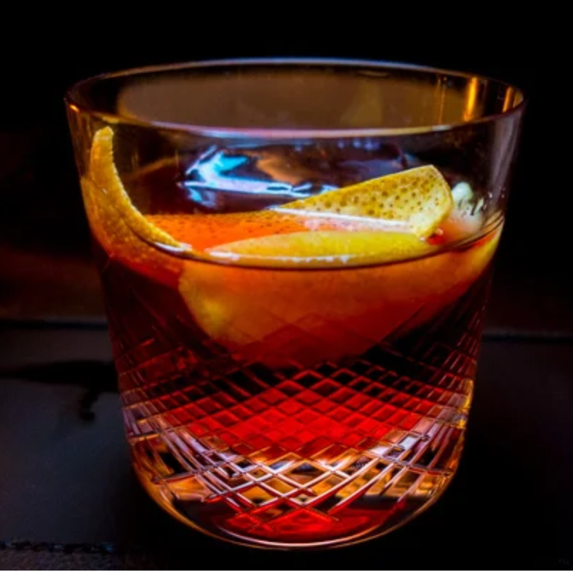 Textured glass with reddish cocktail and citrus peel