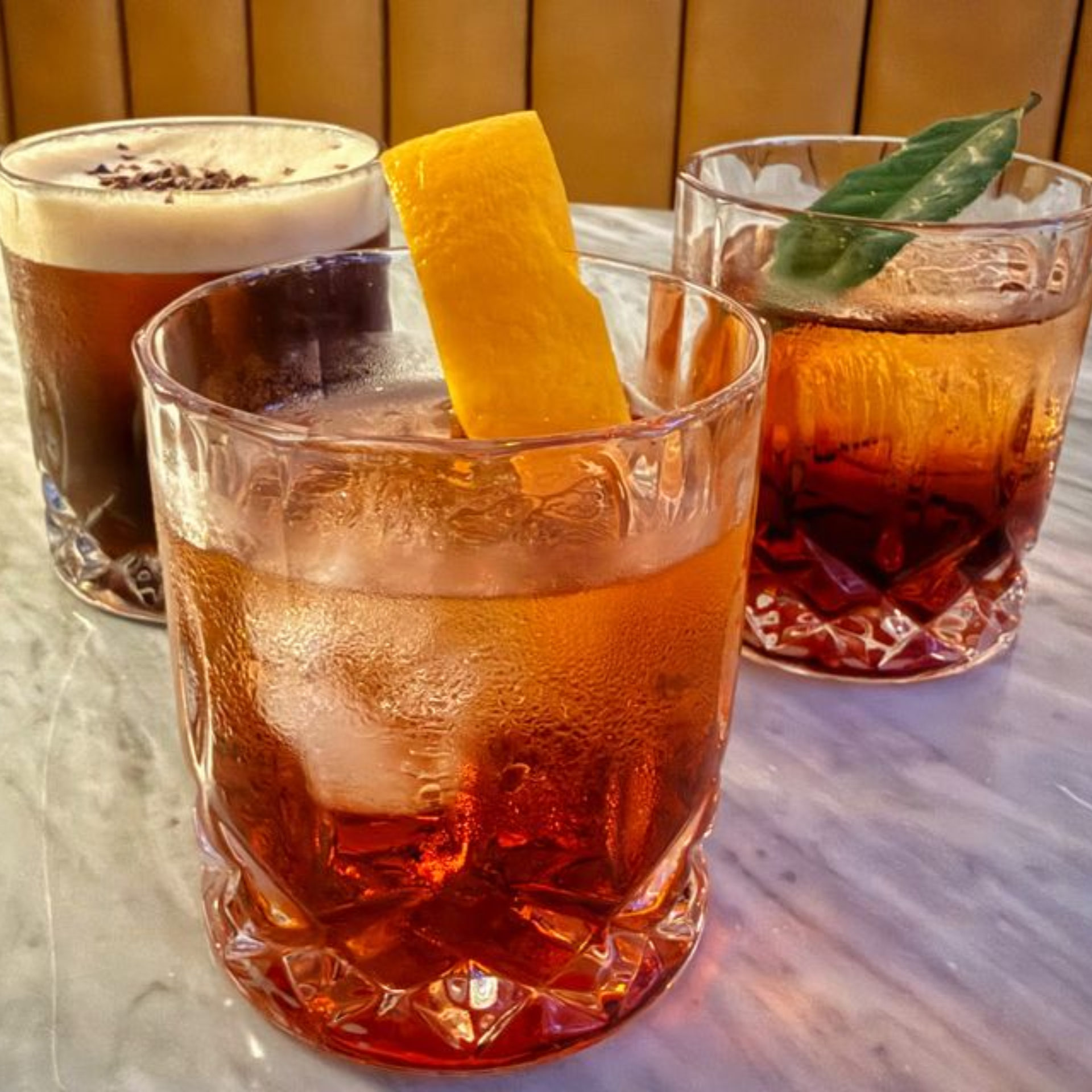 Three cocktails in faceted tumblers with varied garnishes