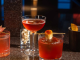 Three colorful cocktails with garnishes on dark bar counter