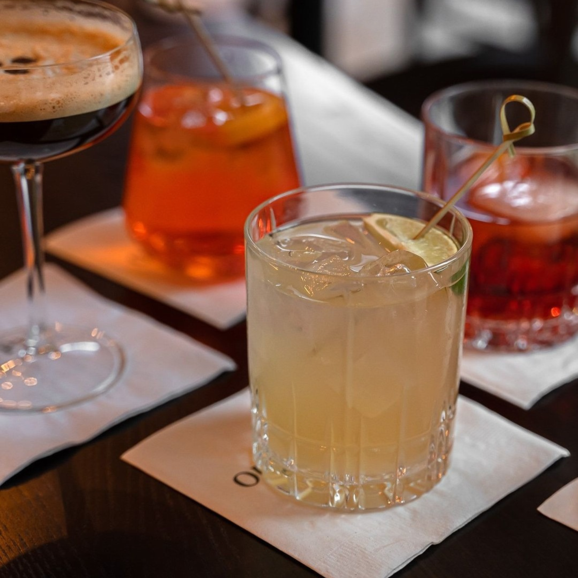 Four varied cocktails on napkins over dark wood surface