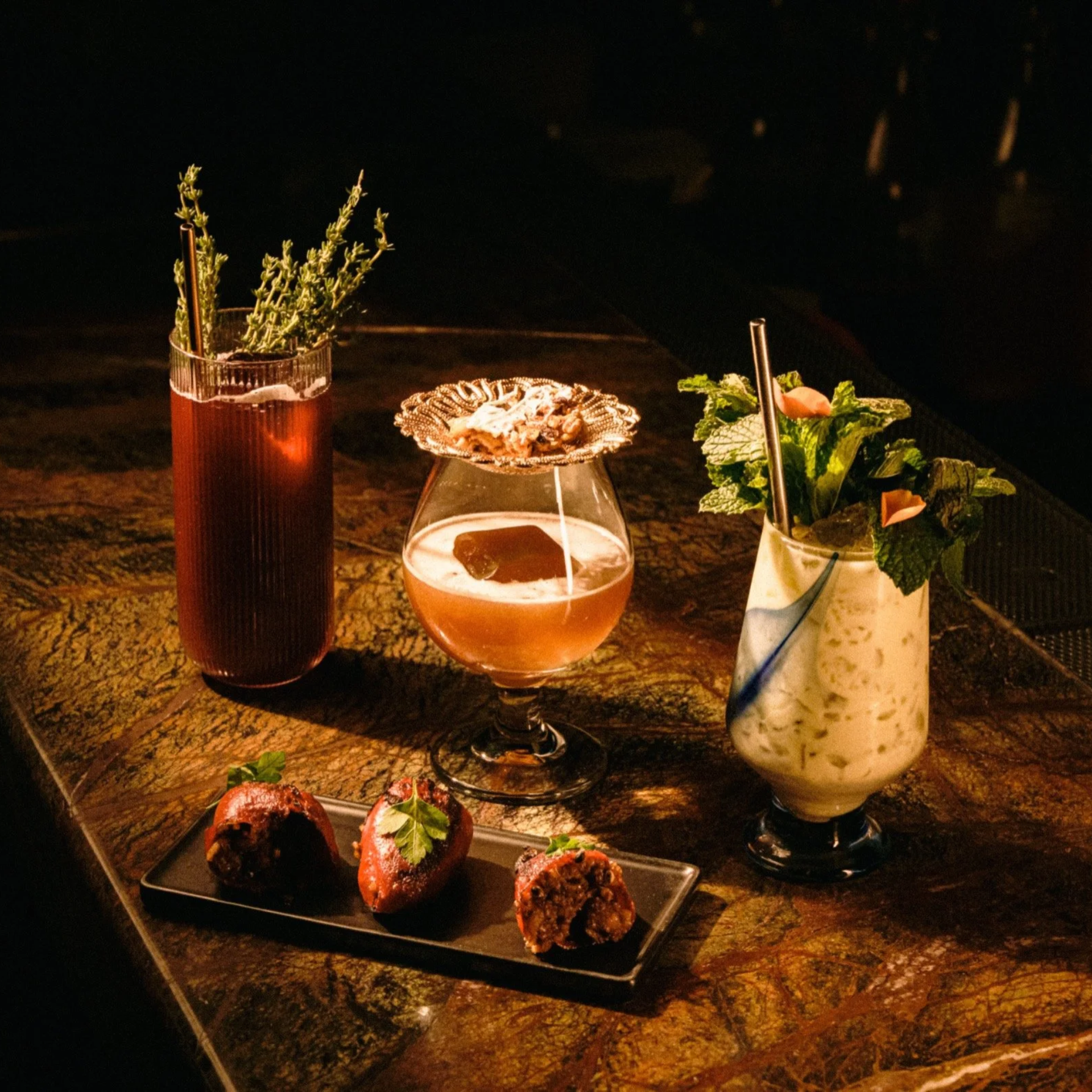 Three craft cocktails with plated appetizers on bar surface